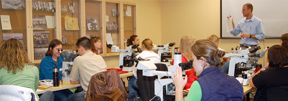 Students in a classroom with microscopes and the instructor sharing notes